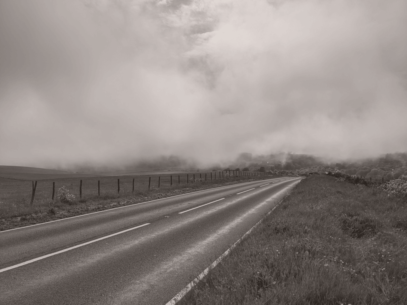 Stretch of road leading to cloudy hills with houses in the horizon